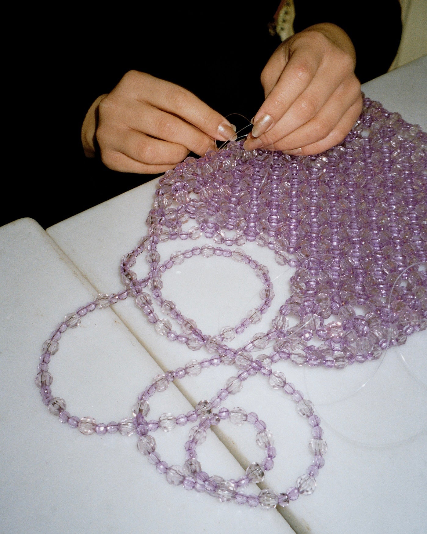 Two hands holding a needle and sewing a handmade beaded bag for Studio 7 Zurich